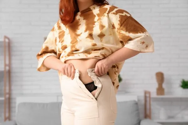 Image of woman trying to do her trousers up after pregnancy weight gain Ravensthorpe