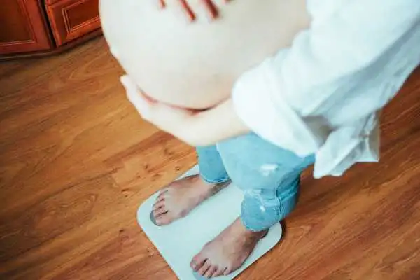 Image of woman weighing herself and experiencing weight gain through pregnancy Ravensthorpe